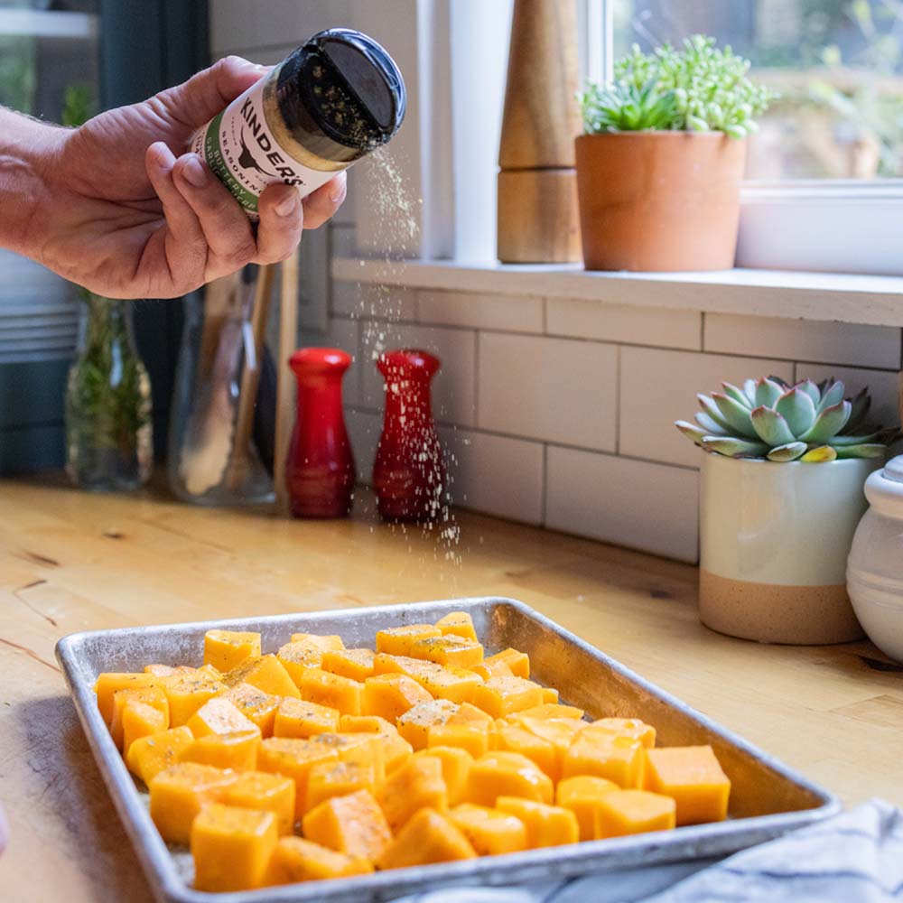 cubed butternut squash being sprinkled with seasoning