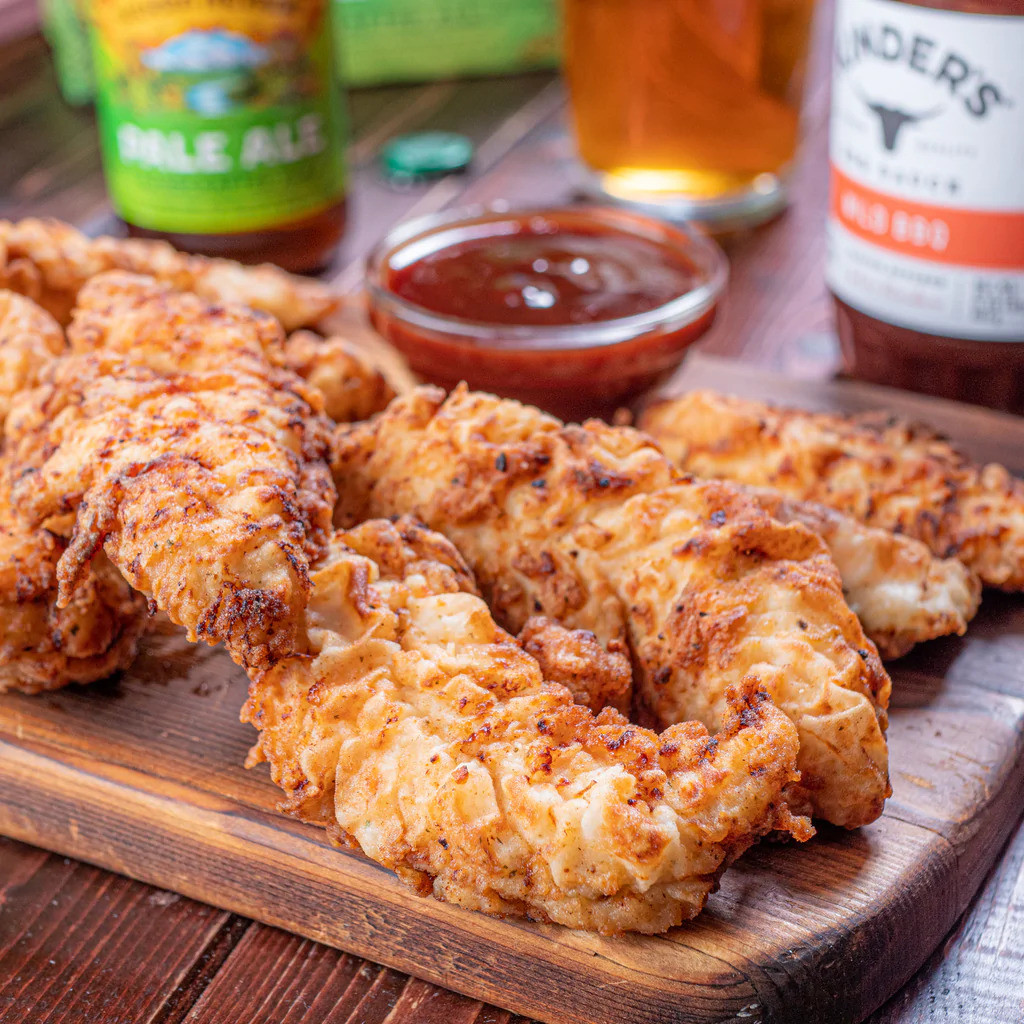 Crispy chicken tenders on a cuttingboard with a bowl of bbq sauce