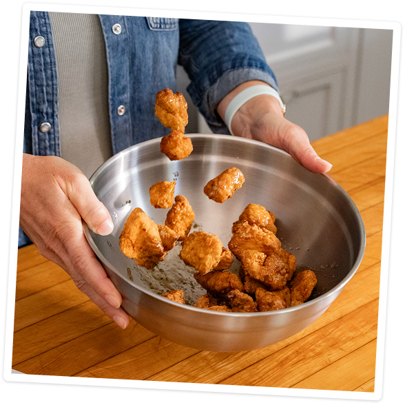 Tossing chicken bites in a metal bowl with Liquid Gold sauce