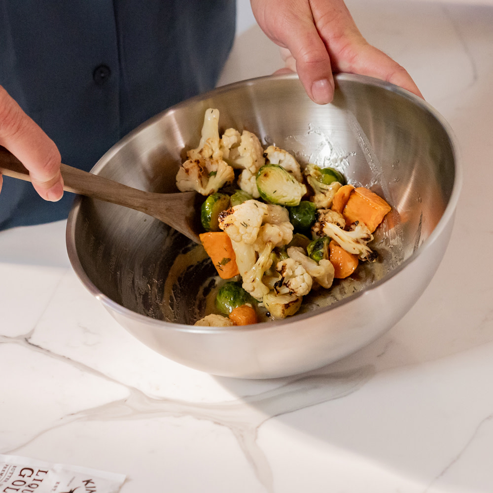 Mixing frozen veggies with Liquid Gold in a metal bowl
