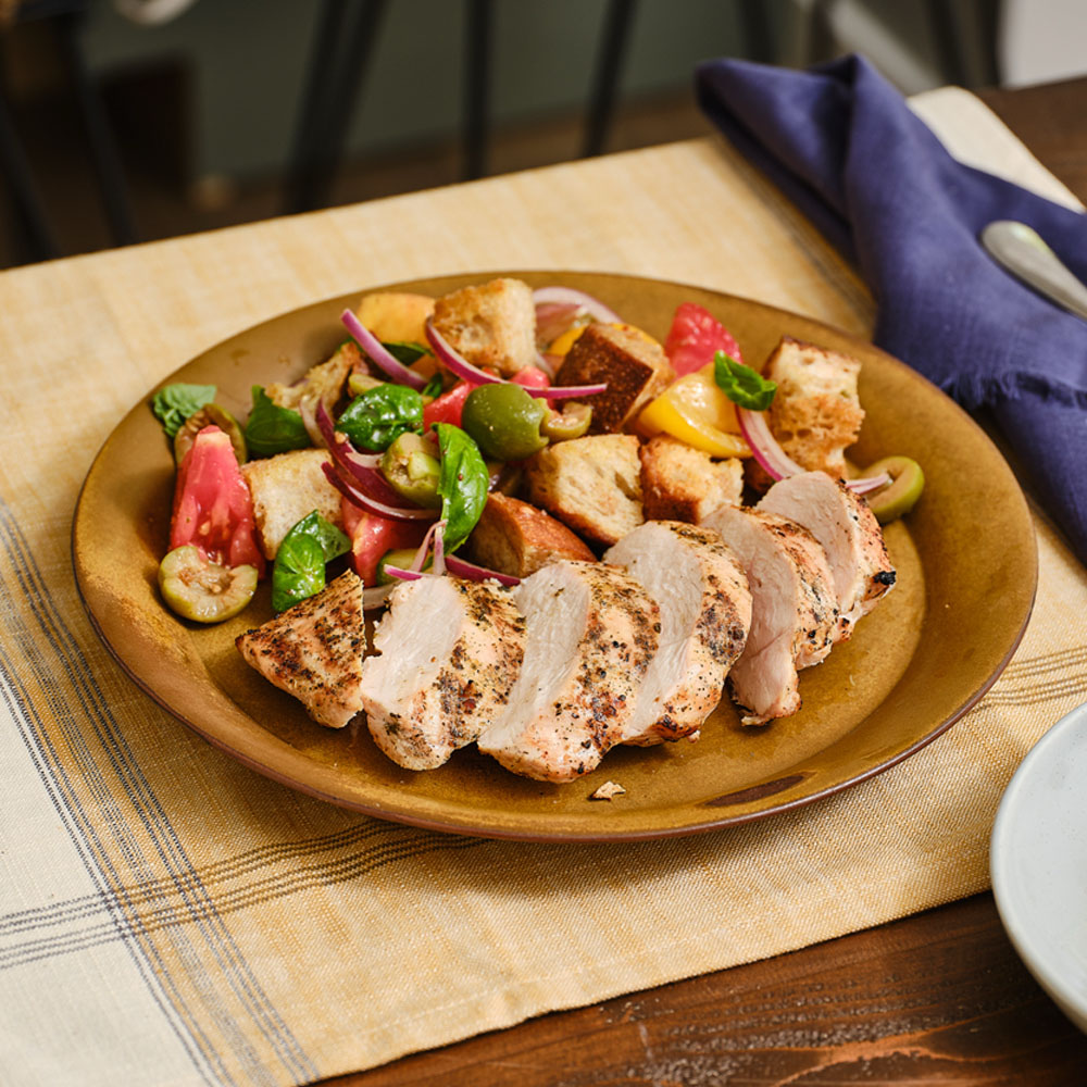 Panzanella salad and sliced chicken breast on a brown plate