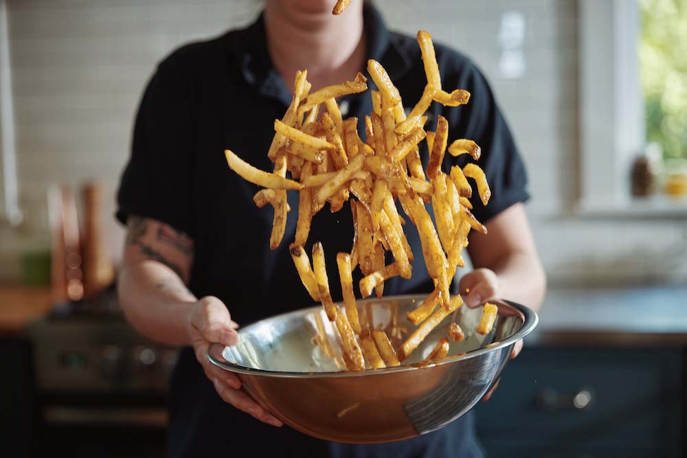 Tossing french fries in seasoning in a metal bowl