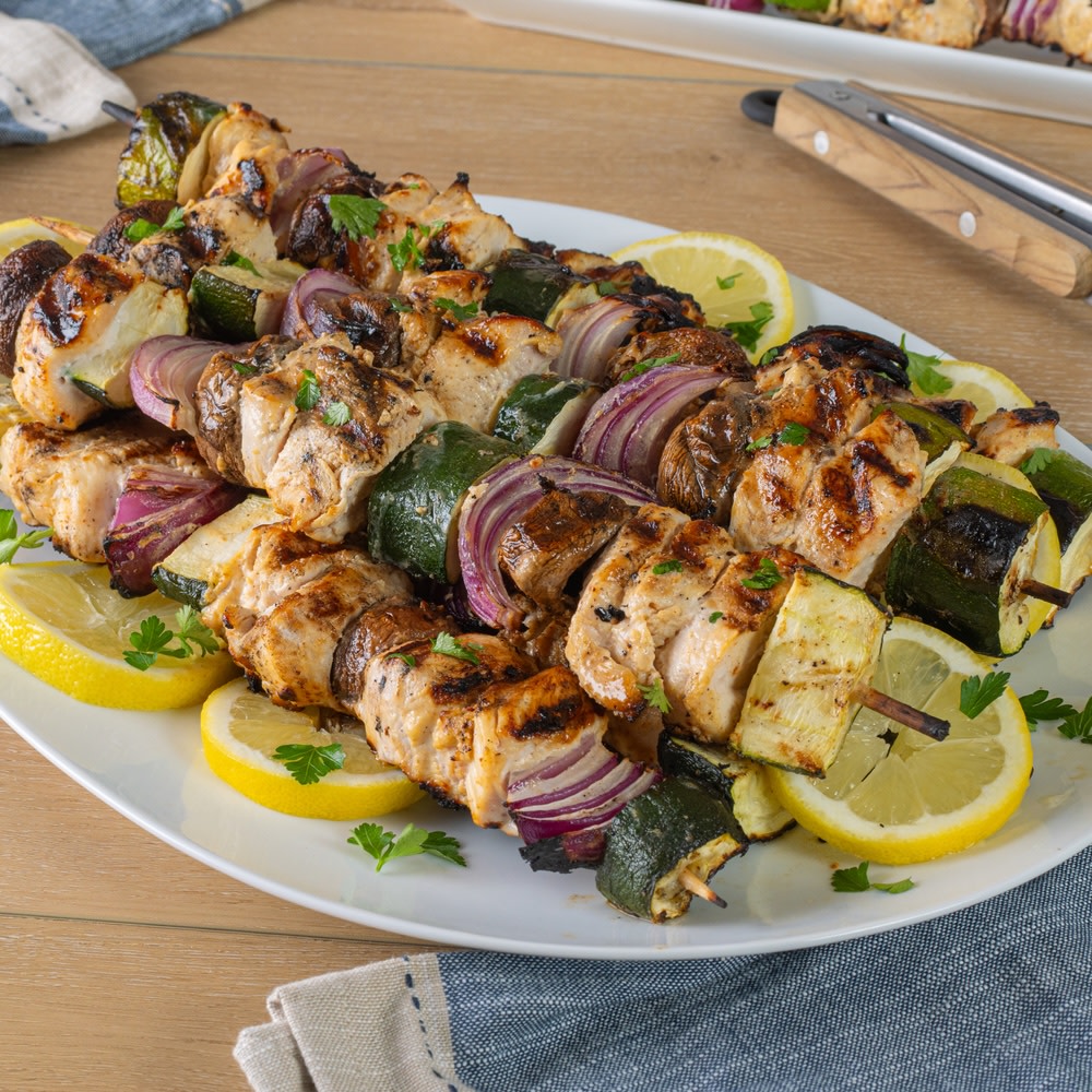 Chicken, zucchini, and onion grilled skewers on a plate with lemons