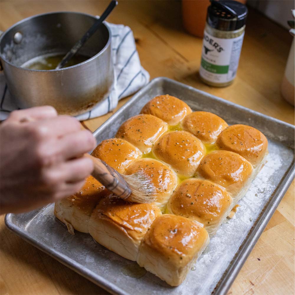 hand brushing butter and seasoning onto premade rolls