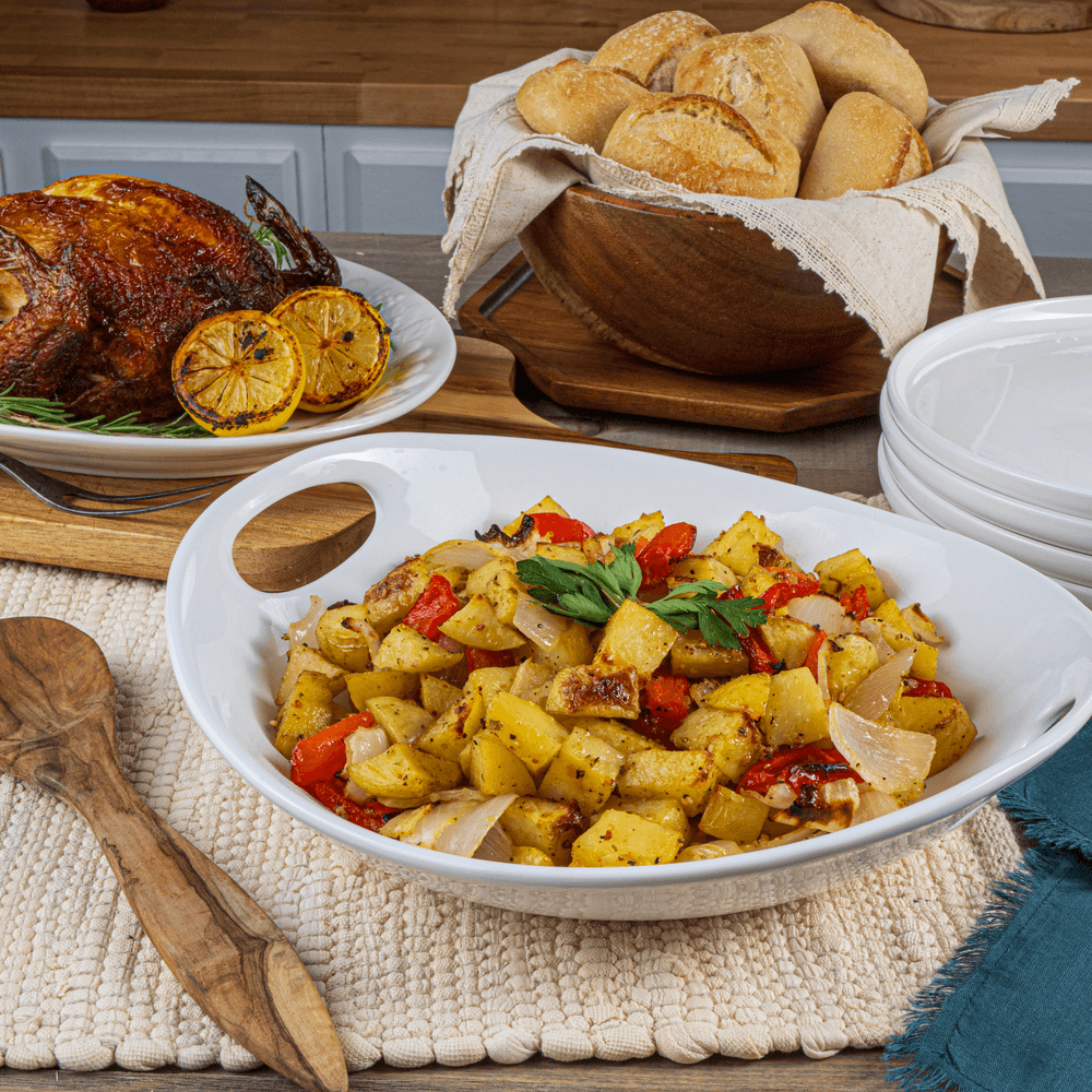 Bowl of roasted potatoes with red peppers on table with roasted turkey and bread rolls