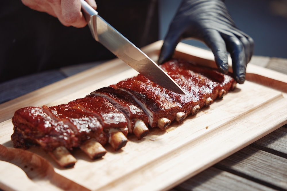 Slicing between the bones of a rested rack of BBQ ribs on the grill