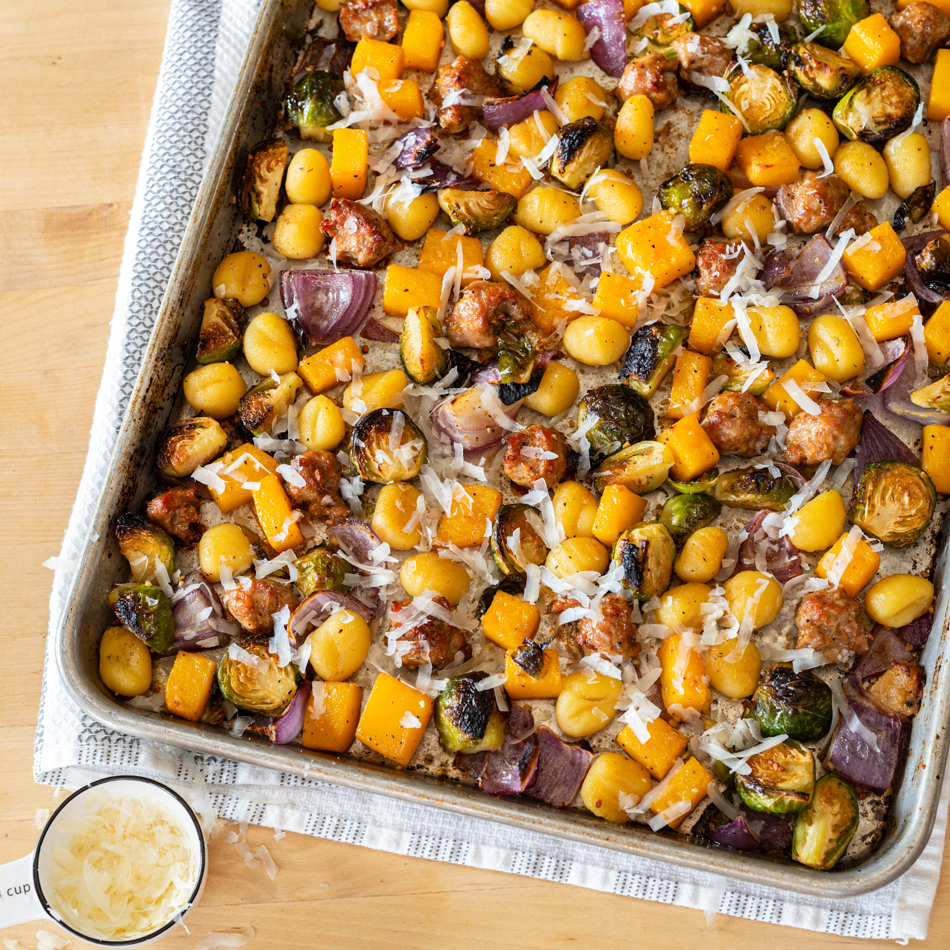 vegetables and sausage on a baking sheet with sprinkled cheese