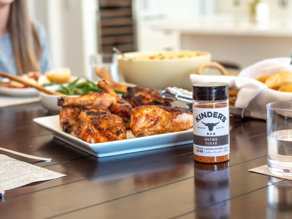 Plate of seasoned grilled chicken on table with bottle of kinder's brown sugar seasoning