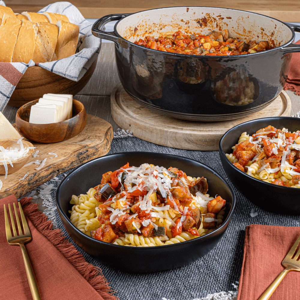 Bowls of vegetable ratatouille over pasta with a large pot of ratatouille