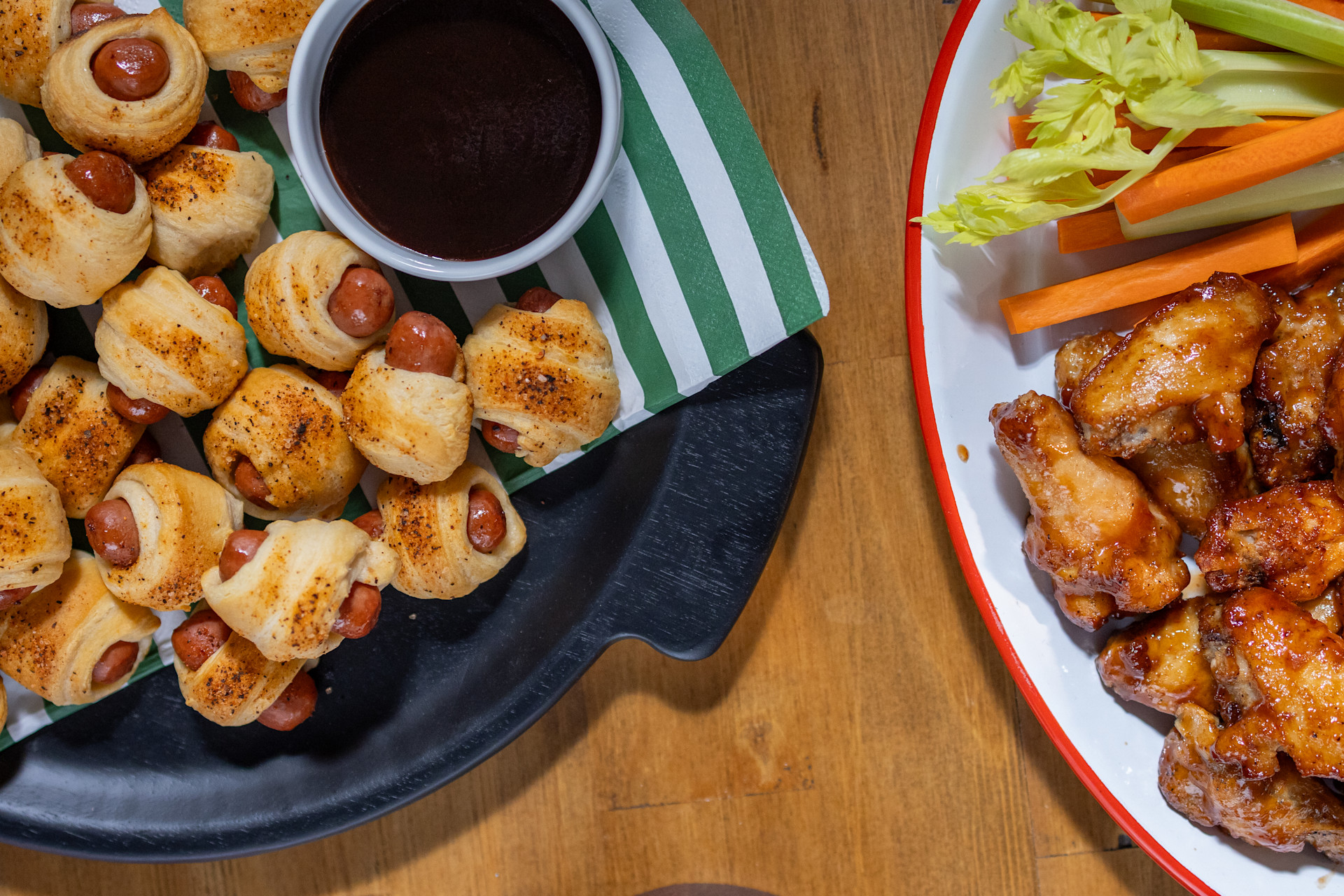 a plate of pigs in a blanket next to a plate of wings