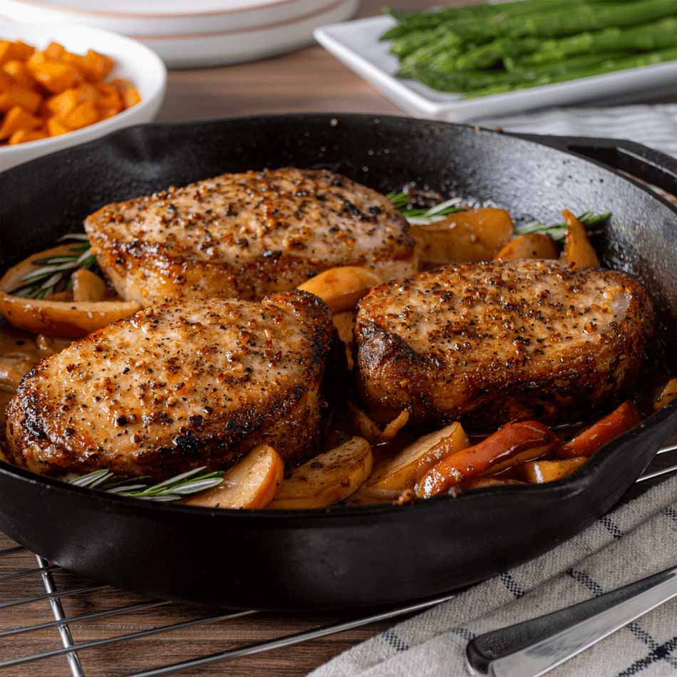 Seasoned porkchops in skillet with cooked apples