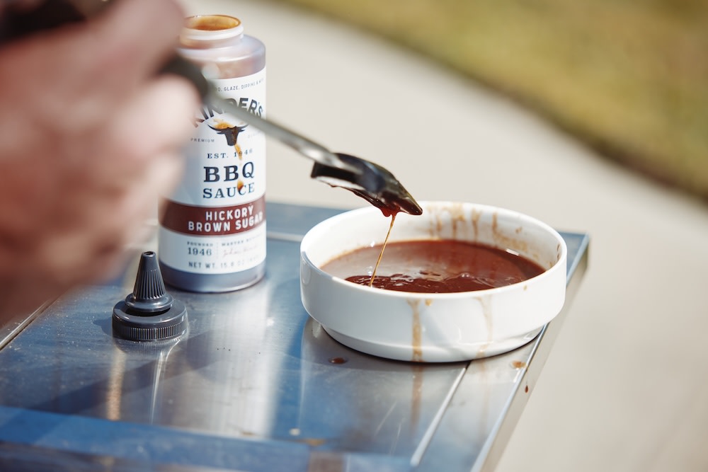 Mixing Kinder’s Hickory Brown Sugar BBQ sauce with rib juices in a small bowl