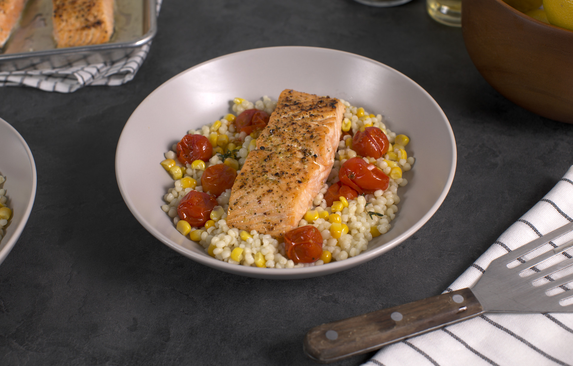 roasted salmon with corn, cherry tomatoes, and couscous in a white bowl