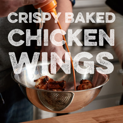 Image of wings being sauced in a bowl with overlay text "Crispy Baked Chicken Wings"