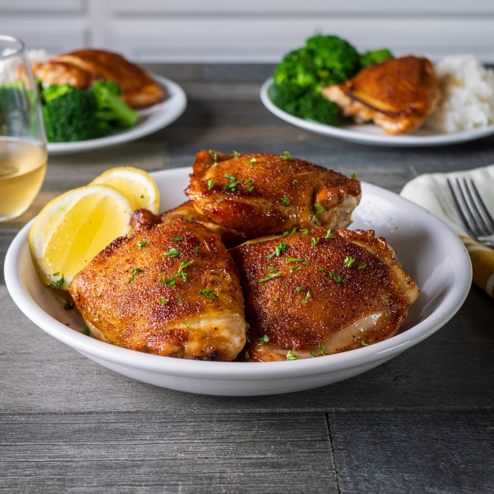 Air fryer chicken thighs on a white serving plate with lemon wedges