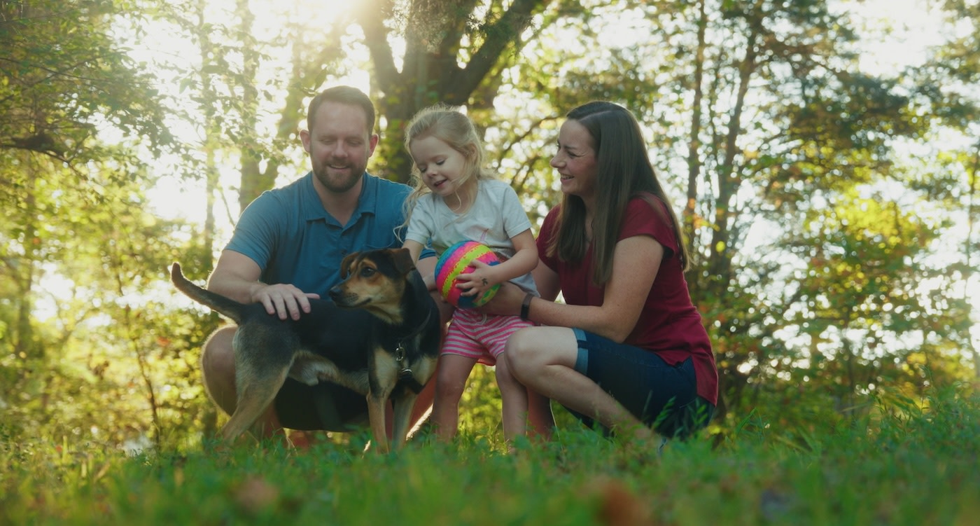 Mother, father, and child petting a dog in a field