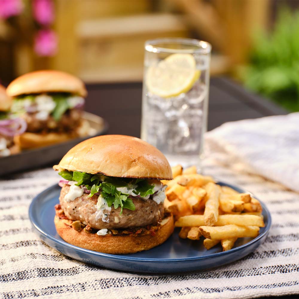 Greek turkey burger on a blue plate with french fries