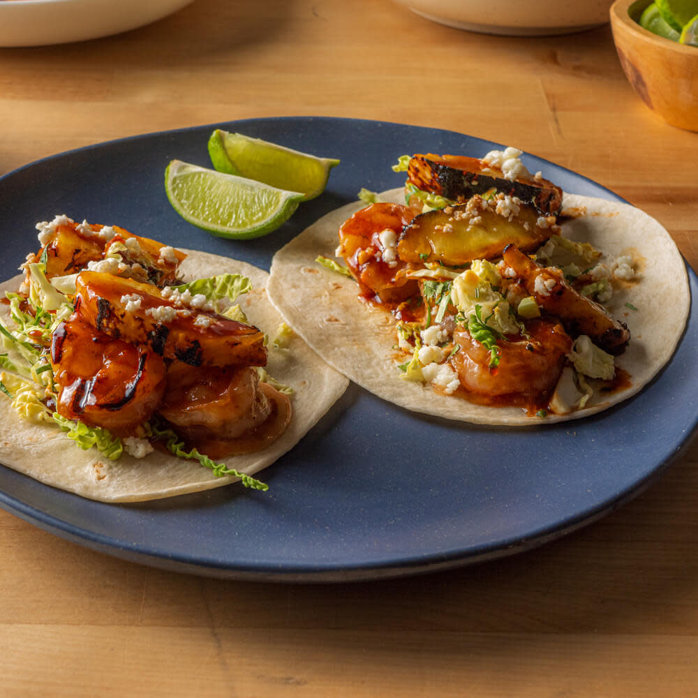 Two shrimp tacos on tortillas with cheese and limes