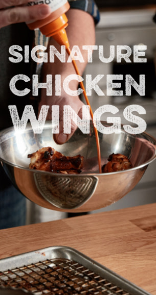 Image of wings being sauced in a bowl with overlay text "Signature Chicken Wings"