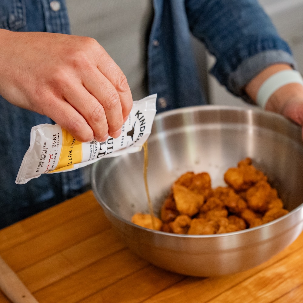 Drizzling Liquid Gold on chicken bites in a metal dish