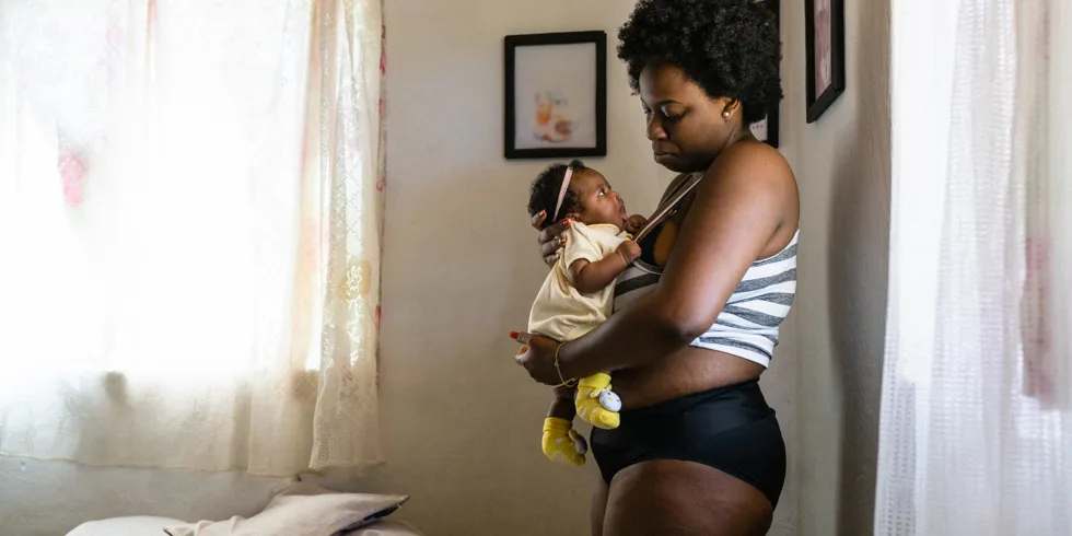 Postpartum other wearing black underwear and holding a young baby