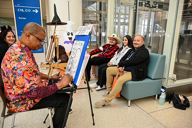 2025 Halloween at MCO photo of three people sitting on a couch getting a caricature picture done.