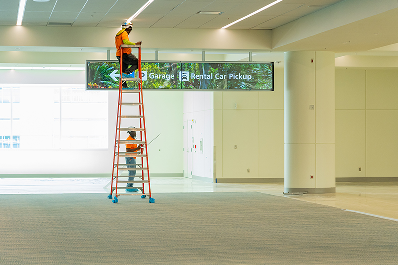 GOAA workers on a ladder installing a new rental car sign.