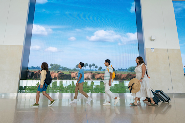 Photo of a family walking down a hallway in Terminal C, with a huge projection screen behind them, displaying horses in a green pasture.