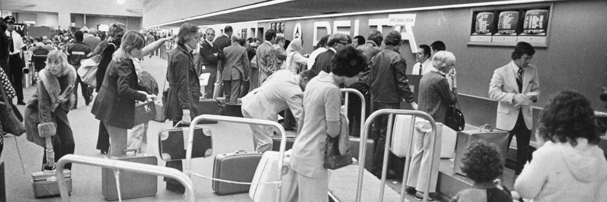 Old black and white 1974 inside photo of Delta airlines ticket counter full of people waiting in line.