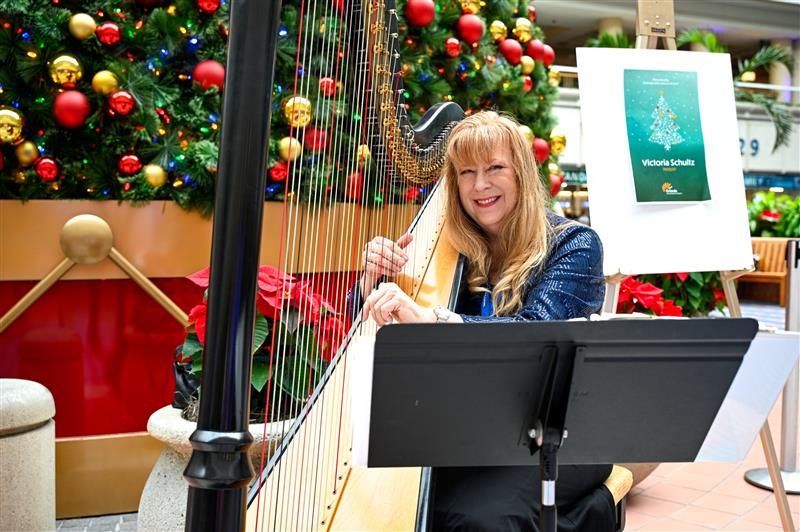 A lady playing a harp at MCO in the atrium by a Christmas tree.