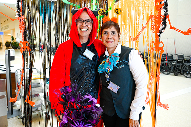 2025 Halloween at MCO photo of two people dressed up in costume. The woman on the left is dressed up in red costume with horns on top of her head. The woman on the right is wearing pumpkin ears on her head.