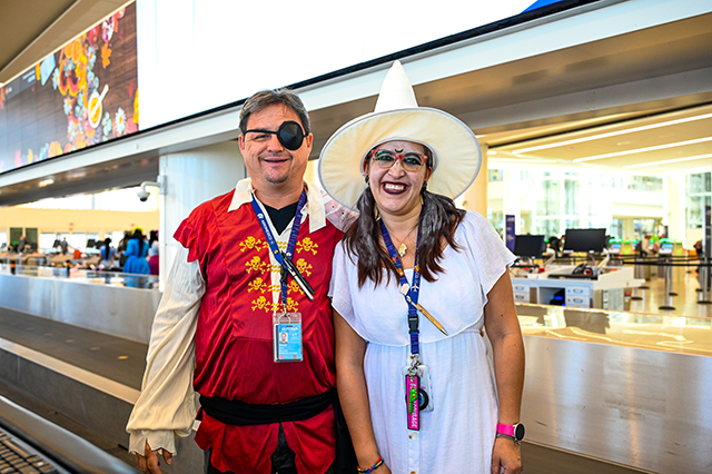 2025 Halloween at MCO photo of two people dressed up in costume. The man on the left is dressed up in a red swashbuckler's outfit. The woman on the right is dressed up as a white witch.