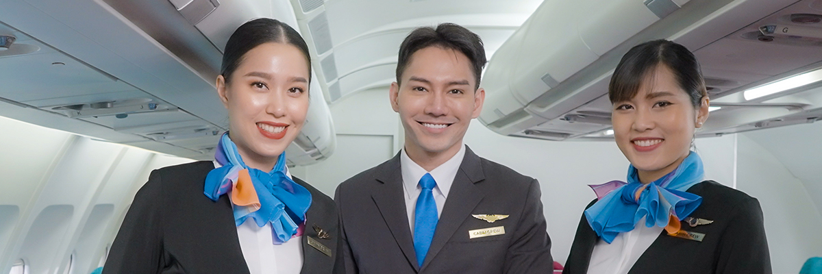 Three cabin crew members in an airplane isle smiling.