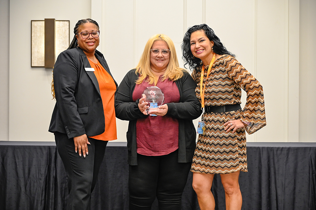 2025 Employee Recognition Brunch photo of three employees. The one in the middle is holding an award.