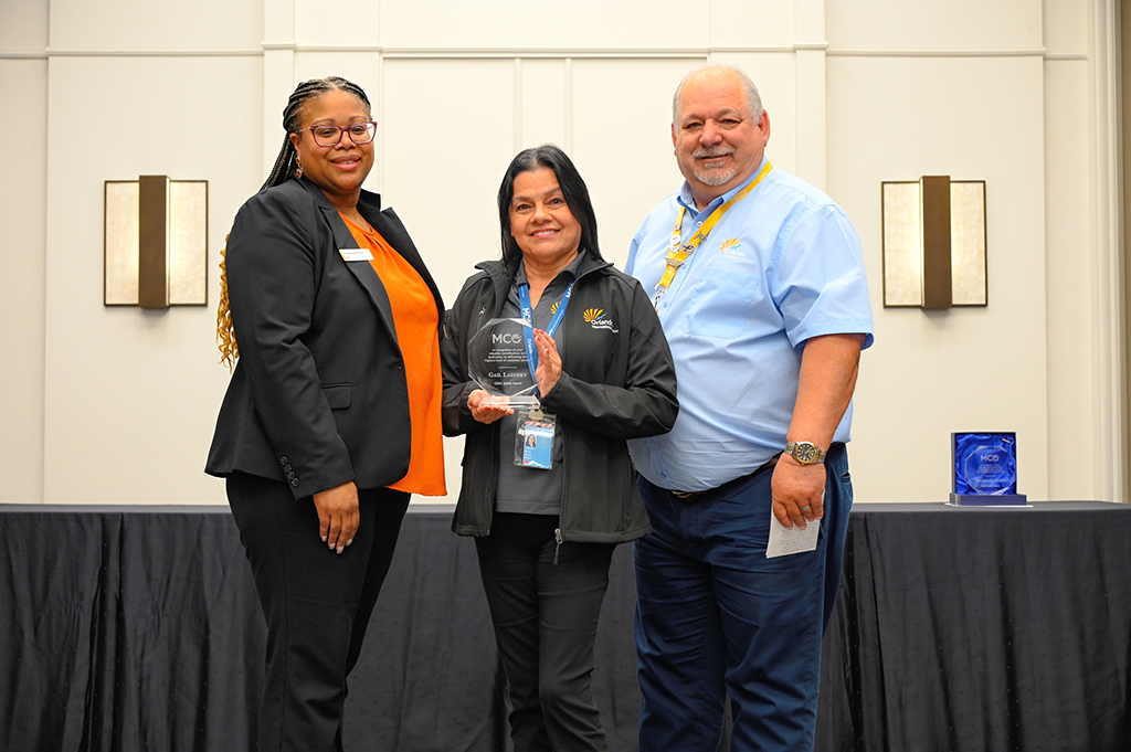 2025 Employee Recognition Brunch photo of three employees. The one in the middle is holding an award.