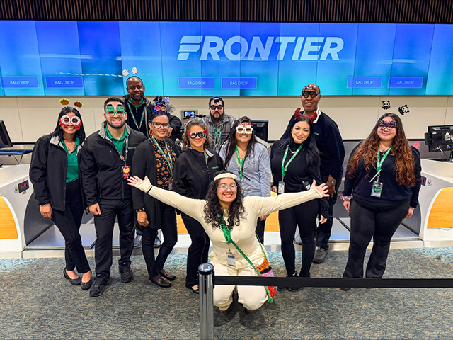 2025 Halloween at MCO group photo of people standing in costume in front of Frontier ticket counter.