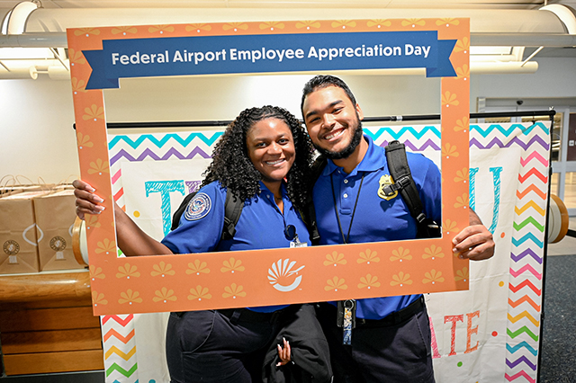 2025 Federal Airport Employee Appreciation Day photo of two federal TSA agents holding a large frame in front that says, "Federal Airport Employee Appreciate Day."