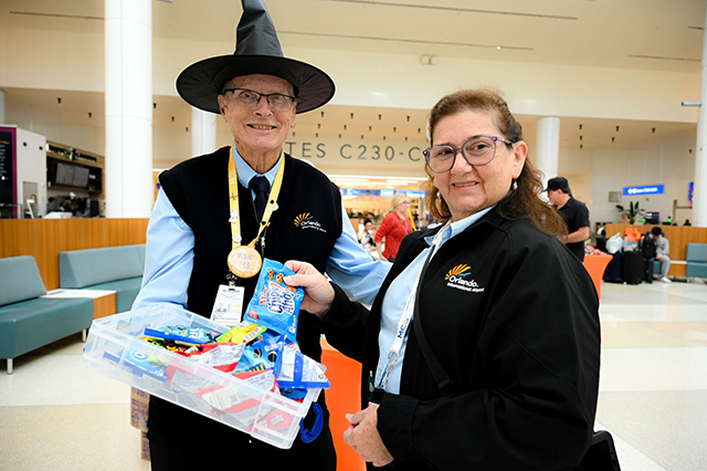 2025 Halloween at MCO photo of two MCO employees handing out candy to travelers. 