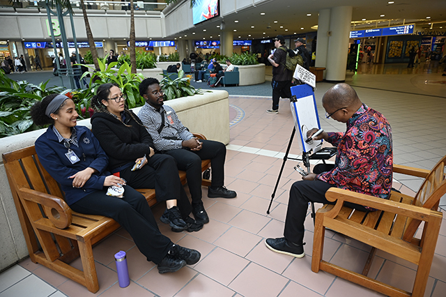 2025 World Kindness Day photo of three people sitting on a bench getting a caricature done.