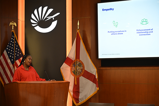 CSAC Culture Team - WORKSHOP Learn and Grow - Compassion Fatigue photo of a display screen showing a slide on empathy. Next to display is a speaker at a podium. 