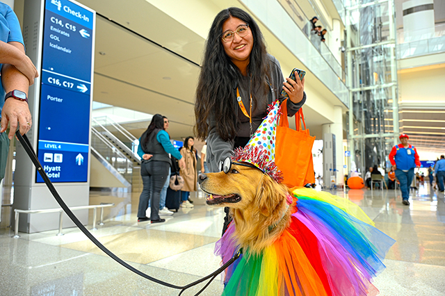 2025 Halloween at MCO photo of a lady petting a Paw Pilots dog dressed up in a clown outfit.