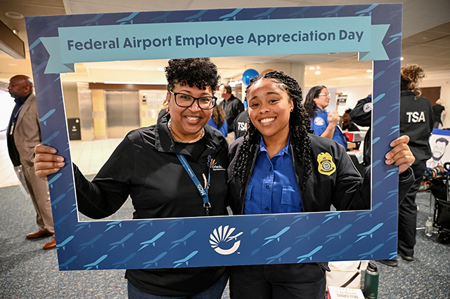 2025 Federal Airport Employee Appreciation Day photo of two federal TSA agents holding a large frame in front that says, "Federal Airport Employee Appreciate Day."