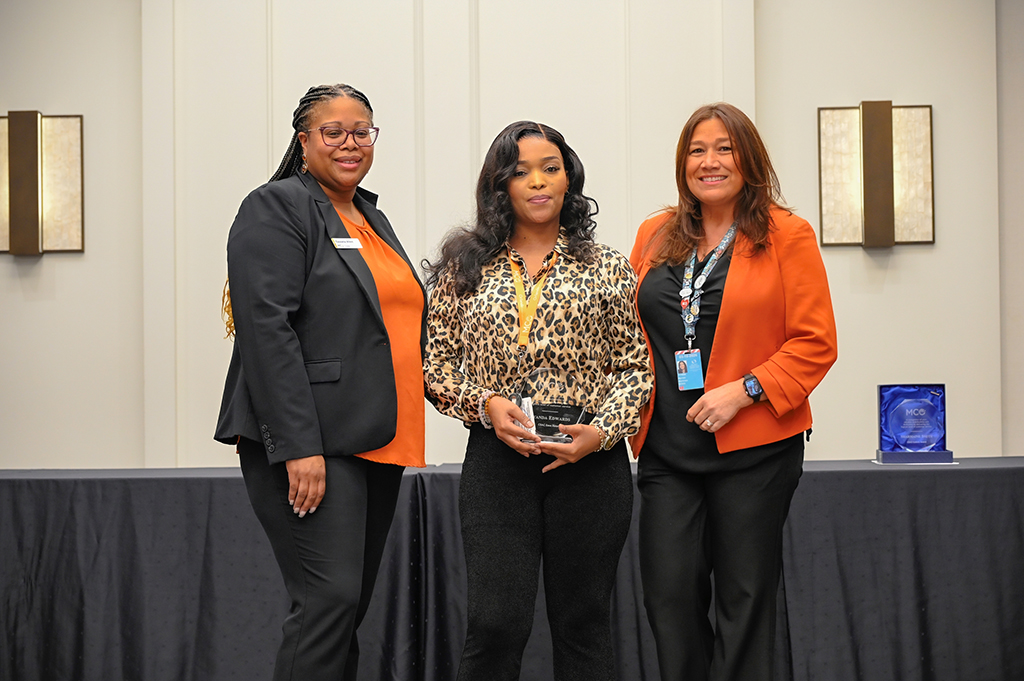 2025 Employee Recognition Brunch photo of three employees. The one in the middle is holding an award.