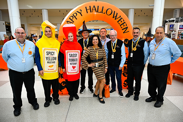 2025 Halloween at MCO group photo of MCO employees standing together in front of an orange blow up "Happy Halloween" arch. 