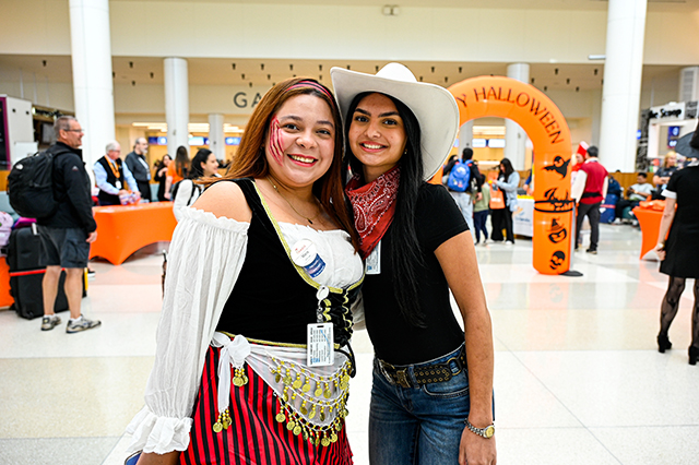 2025 Halloween at MCO photo of two ladies dressed up. The lady on the left is dressed up as a dancer. The lady on the right is dressed up in a western outfit.