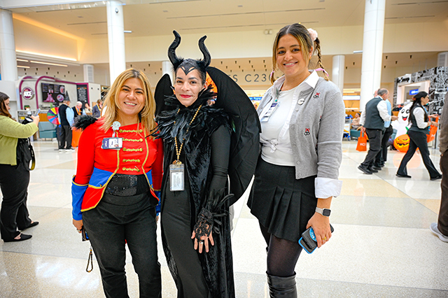 2025 Halloween at MCO photo three ladies dressed up in costume. One on the left is dressed as a nutcracker.  The one in the center is dressed as a witch. The one on the right is dressed as a cheerleader.