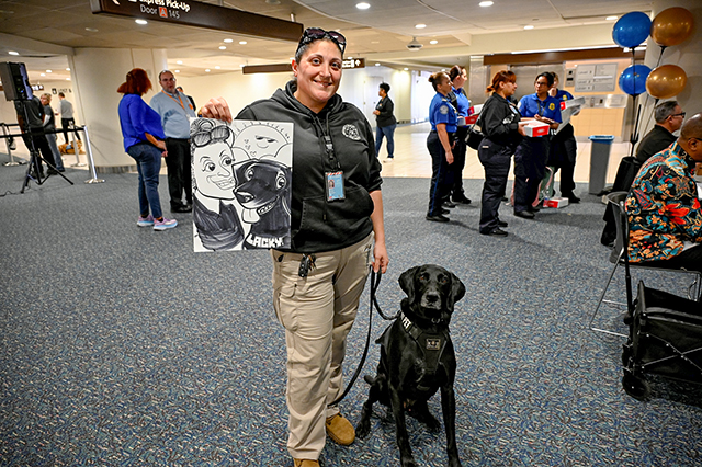 2025 Federal Airport Employee Appreciation Day photo of a security worker showing a caricature drawing of her and her black dog.