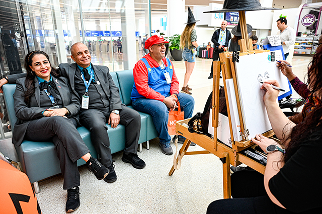 2025 Halloween at MCO photo of two people sitting on a couch getting a caricature picture drawn.