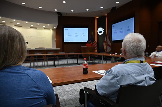 CSAC Culture Team - WORKSHOP Learn and Grow - Compassion Fatigue photo of two GOAA employees sitting at table looking at the speaker at the podium.