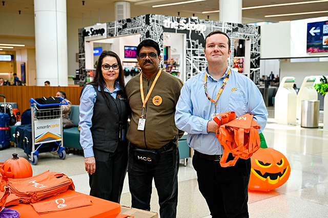 2025 Halloween at MCO photo three people handing out orange MCO bags.